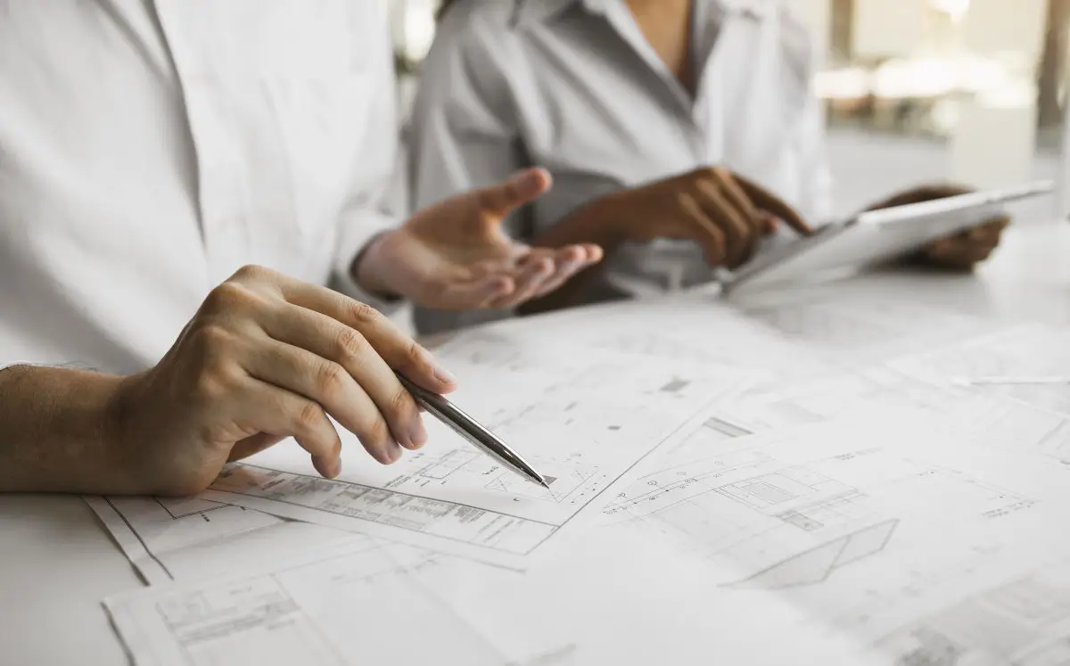 Two professionals reviewing and discussing plans or blueprints on a desk, symbolizing modifications and adjustments in Chapter 13 bankruptcy plans.